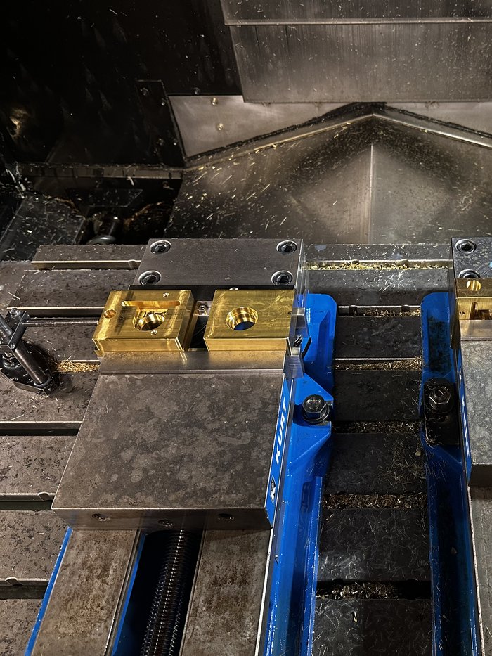 Machined brass components held in a vise inside a CNC mill